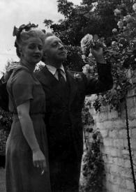 Portada:Plano general de Aniela Rubinstein posando junto a Arthur Rubinstein observando una flor