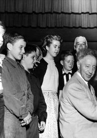 Portada:Plano general de Arthur Rubinstein, sentado al piano, y un hombre rodeado por un grupo de niños posando