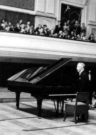 Portada:Plano general de Arthur Rubinstein de pie junto al piano, saludando al publico sentado en el escenario