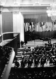 Portada:Plano general del escenario: Arthur Rubinstein (perfil derecho) sentado al piano, detrás la orquesta, delante el público. Fotografía tomada desde el fondo de la sala de conciertos