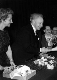 Portada:Plano medio de Aniela Rubinstein y Arthur Rubinstein (perfil derecho), en la mesa de la presidencia, estrechando la mano a una mujer