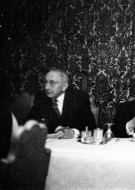 Portada:Plano medio de Arthur Rubinstein con un puro en la mano, charlando con un hombre sentados en una mesa