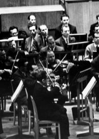 Portada:Plano general de la orquesta, con Arthur Rubinstein (perfil derecho) sentado al piano y el público de la sala de conciertos.