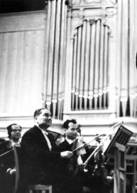 Portada:Plano general de Arthur Rubinstein saludando al público desde el escenario con la orquesta detrás