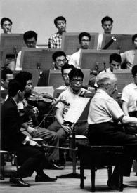 Portada:Plano general de Arthur Rubinstein (perfil derecho) sentado al piano durante un ensayo, con la orquesta en segundo plano y Seijko Ozawa dirigiendo la orquesta