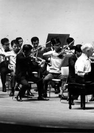 Portada:Plano general de Arthur Rubinstein (perfil derecho) sentado al piano durante un ensayo, con la orquesta en segundo plano y Seijko Ozawa dirigiendo la orquesta