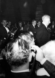 Portada:Plano medio de Arthur Rubinstein (perfil derecho) de pie, junto al piano con la orquesta detrás