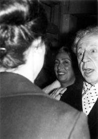 Portada:Plano medio de Arthur Rubinstein charlando con una mujer (de espaldas), al fondo otra mujer observándole