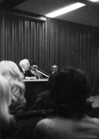 Portada:Plano medio de Arthur Rubinstein hablando a través de un micrófono junto a otras personas sentadas