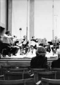 Portada:Plano medio de espaldas de J. Philippe Collard, Arthur Rubinstein y Aniela Rubinstein, sentados en el patio de butacas, escuchándo a la orquesta