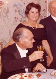 Portada:Plano medio de un hombre sentado en una mesa brindando con Arthur  Rubinstein, detrás, de pie y posando una mujer y un hombre