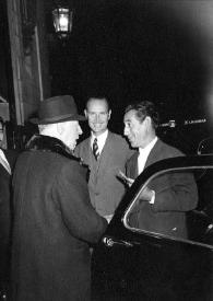 Portada:Plano general de Arthur Rubinstein de espaldas (perfil derecho) saludando a dos hombres junto a un coche con las puertas  abiertas