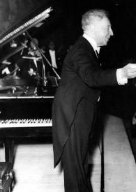 Portada:Plano general de Arthur Rubinstein (perfil derecho), de pie, saludando al público junto al piano
