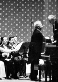 Portada:Plano general del director de la orquesta (perfil derecho) saludando a Arthur Rubinstein (medio perfil izquierdo) al fondo la orquesta