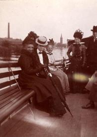 Portada:Plano general de una mujer, un hombre, Señora de Hartzell, una mujer, un hombre, una mujer y Señora Rosentower posando sentado en una barca navegando por un río
