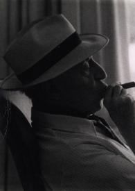 Portada:Plano medio de Arthur Rubinstein (perfil derecho) con sombrero, sentado fumando un puro
