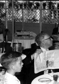 Portada:Plano medio de Arthur Rubinstein, con el periódico, hablando con un camarero. John rubinstein y Alina Rubinstein sentados a la mesa