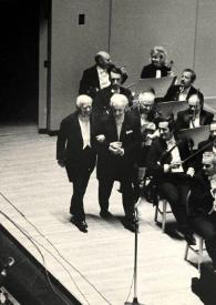 Portada:Plano general de Eugène Ormandy y Arthur Rubinstein caminando desde un lateral del escenario hacia el centro, detrás la orquesta les observa