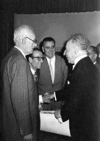 Portada:Plano general de Arthur Rubinstein (perfil izquerdo) saludando a tres hombres